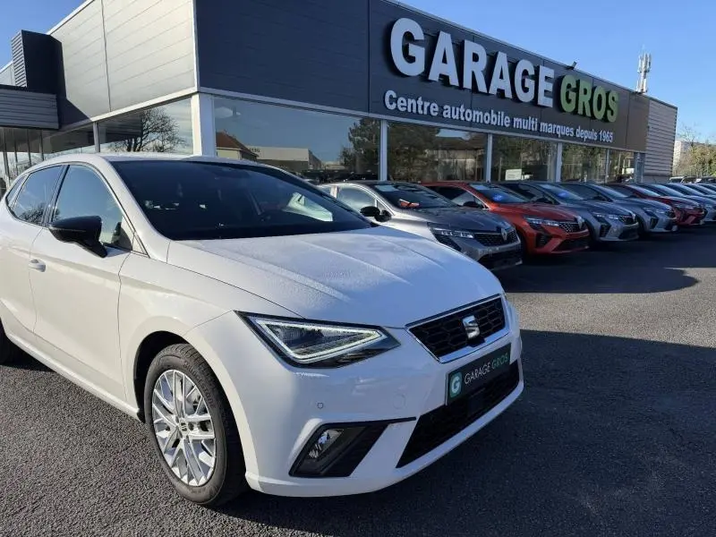 SEAT Ibiza 1.0 TSI 115cv FR blanc Nevada métallisé vue 3/4 avant droit devant un garage multimarques.