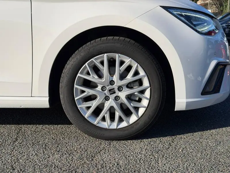 Gros plan sur la roue avant droite d'une SEAT Ibiza 2025 blanche Nevada métallisée, avec jante alliage au design étoilé.