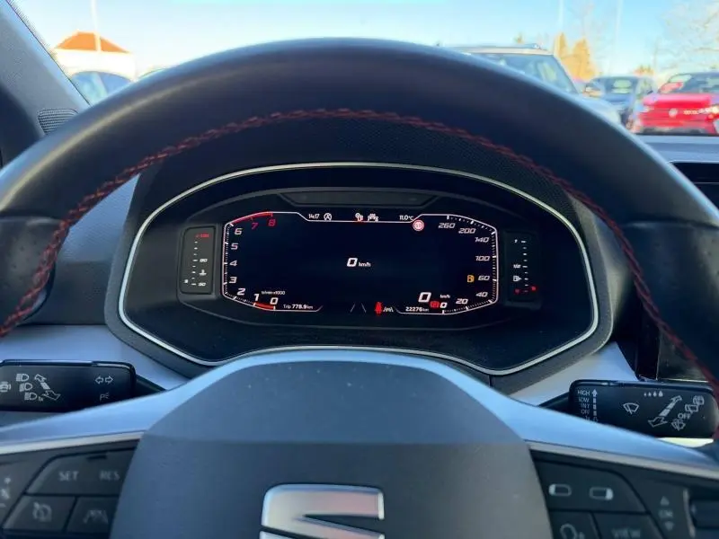 Vue depuis le poste de conduite du tableau de bord numérique de la SEAT IBIZA 1.0 TSI FR 2025 en blanc Nevada métallisé.