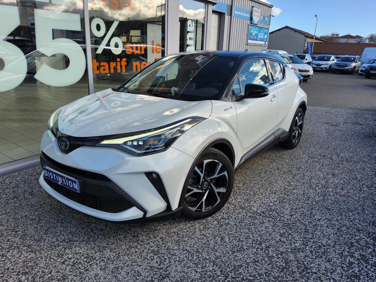 Toyota C-HR blanc nacré en 3/4 avant droit, avec jantes alliage noires et toit noir brillant visible.