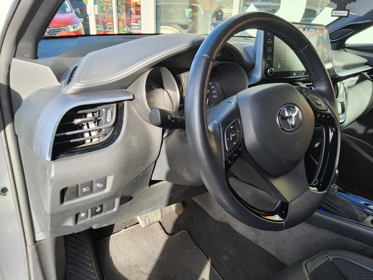 Vue intérieure côté conducteur du Toyota C-HR blanc nacré 2020, volant cuir multifonction et tableau de bord moderne.