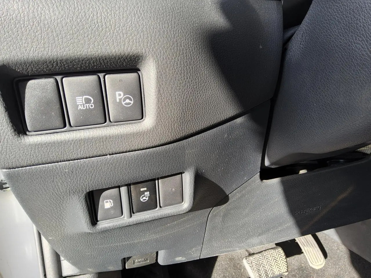 Gros plan sur les commandes côté conducteur du Toyota C-HR blanc nacré, avec boutons d'assistance et réglages divers.