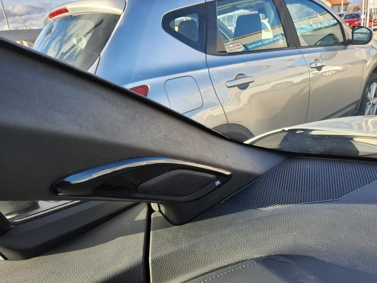 Vue intérieure côté droit sur l'enceinte JBL et la portière, avec une Toyota C-HR blanc nacré visible à l'extérieur.