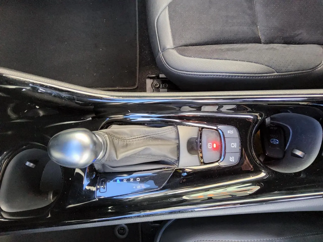 Vue rapprochée de la console centrale noire brillante avec levier de vitesse automatique et siège tissu gris du Toyota C-HR hybride.