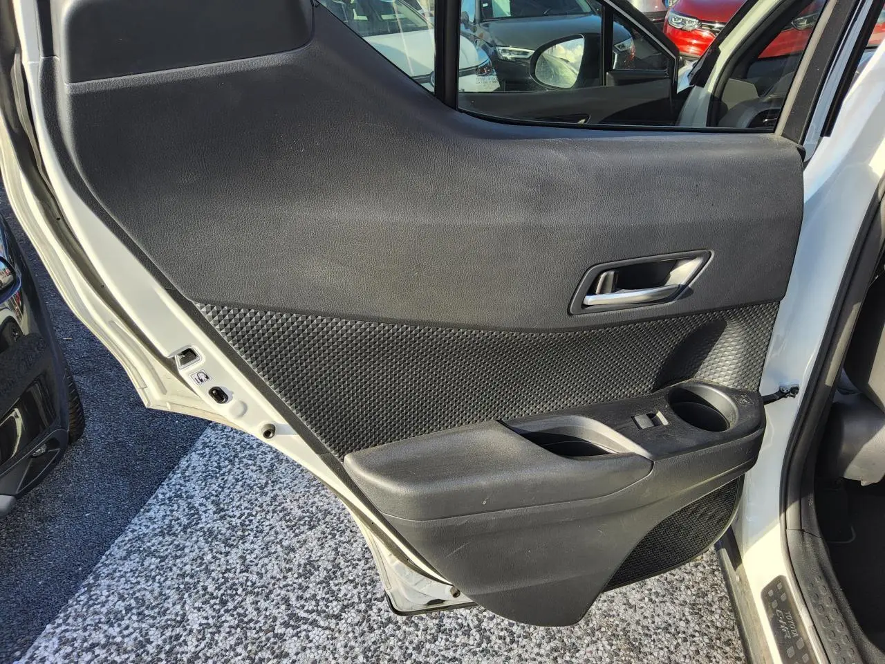Vue intérieure de la porte arrière droite d’un Toyota C-HR blanc nacré, avec garniture noire texturée et poignée argentée.