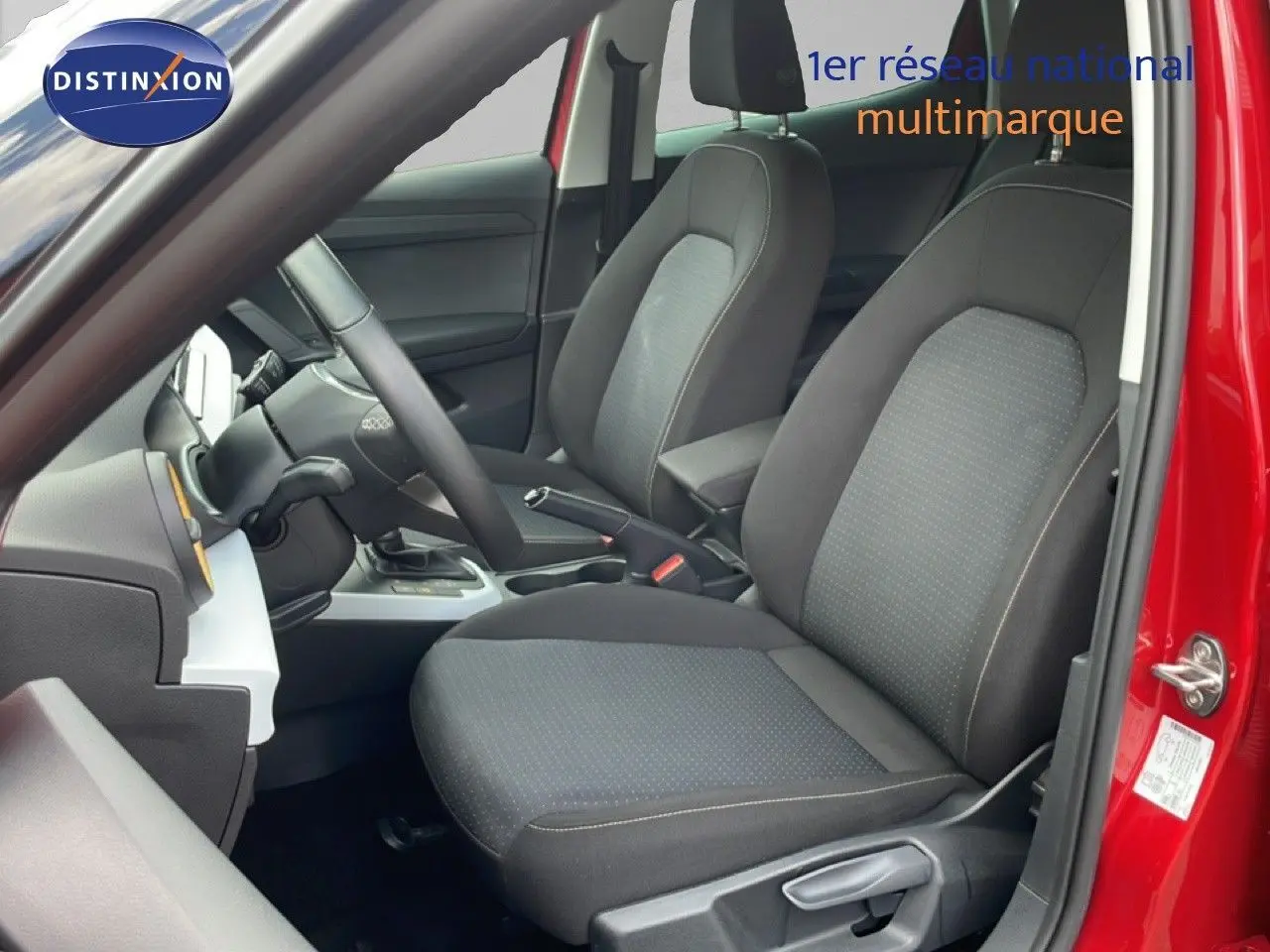 Vue intérieure côté conducteur du SEAT Arona rouge désir métal, mettant en valeur les sièges tissu noirs et le volant multifonction.