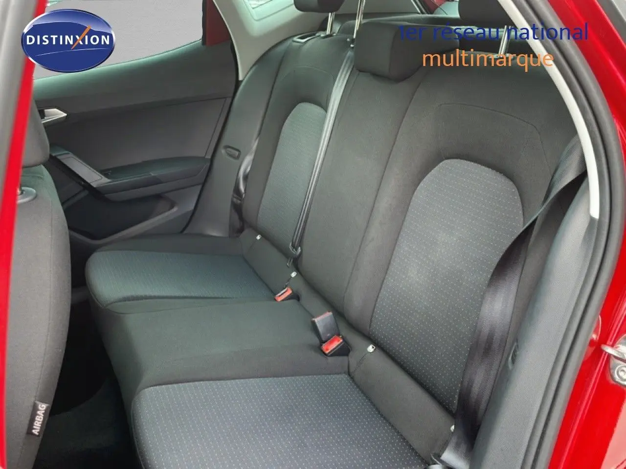Vue intérieure sur la banquette arrière du SEAT Arona rouge désir métal, avec sièges en tissu noir et ceinture de sécurité visible.