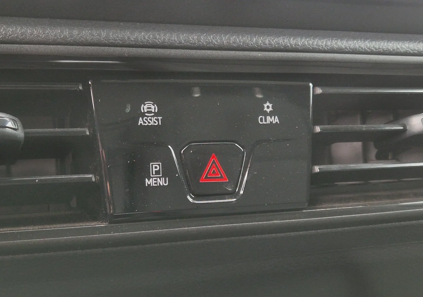 Gros plan sur la console centrale noire du Volkswagen Caddy blanc 2023, avec bouton de signalisation d’urgence rouge et commandes assist et clima.