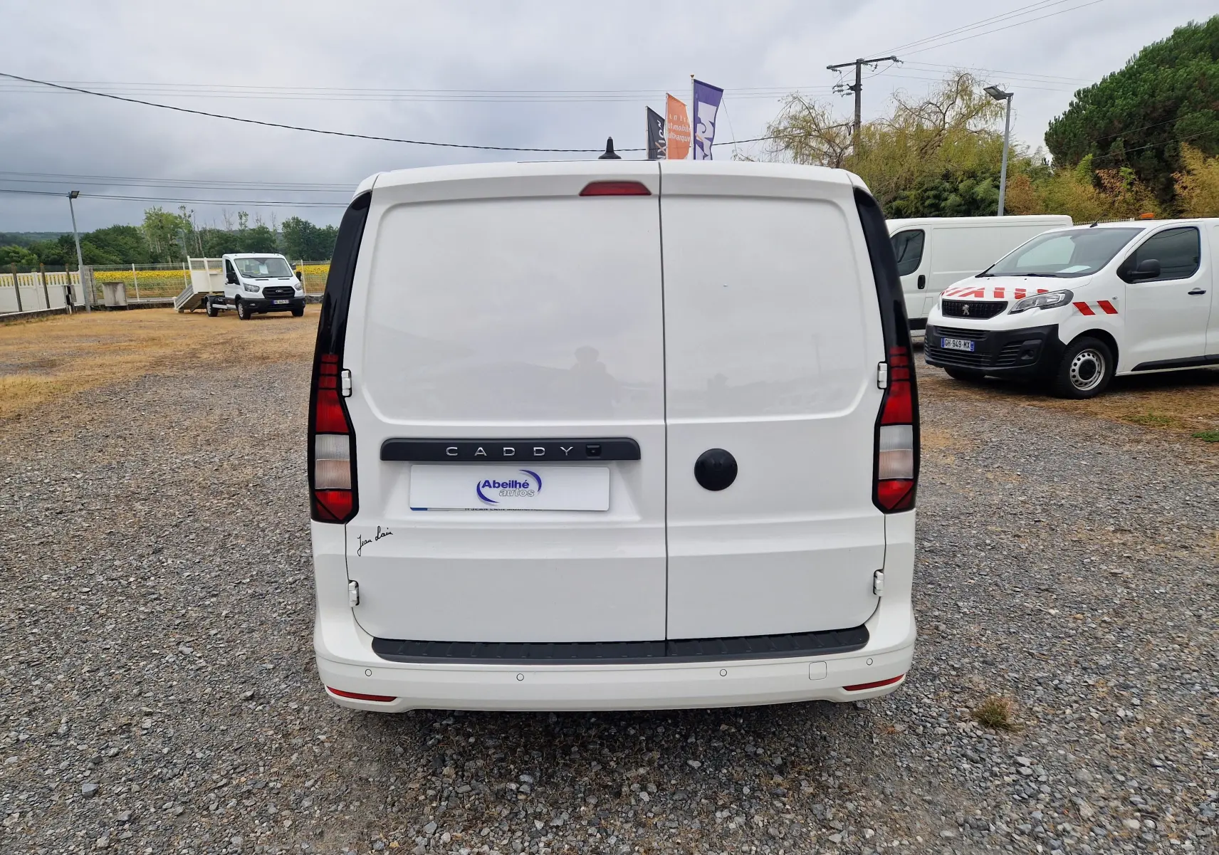 Vue arrière d'un utilitaire Volkswagen Caddy Cargo blanc 2023, portes battantes fermées, sur un sol gravillonné.