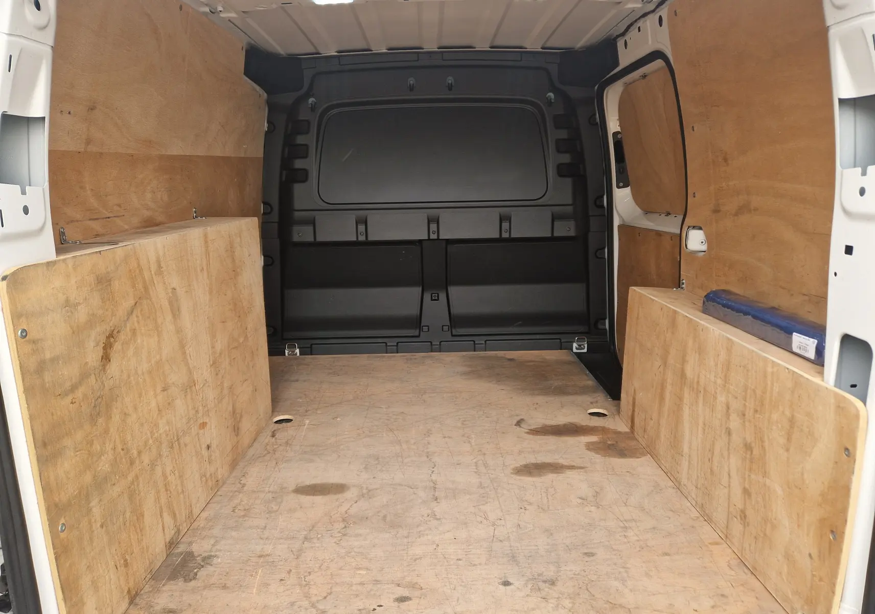 Vue intérieure arrière du Volkswagen Caddy Cargo blanc 2023, montrant l'espace de chargement avec revêtement bois.