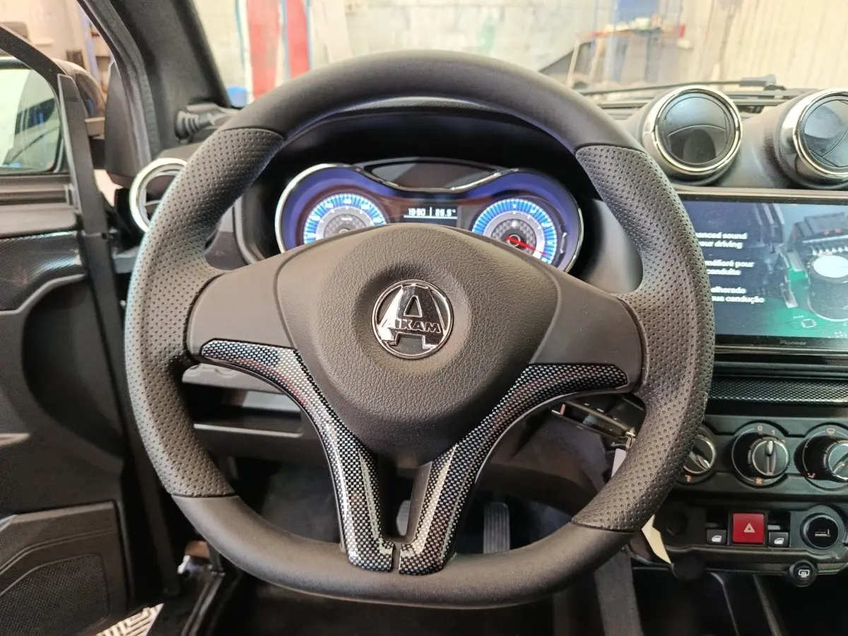 Vue intérieure centrée sur le volant noir perforé de l'AIXAM Ambition 0.5 City Coupe GTI avec tableau de bord lumineux.