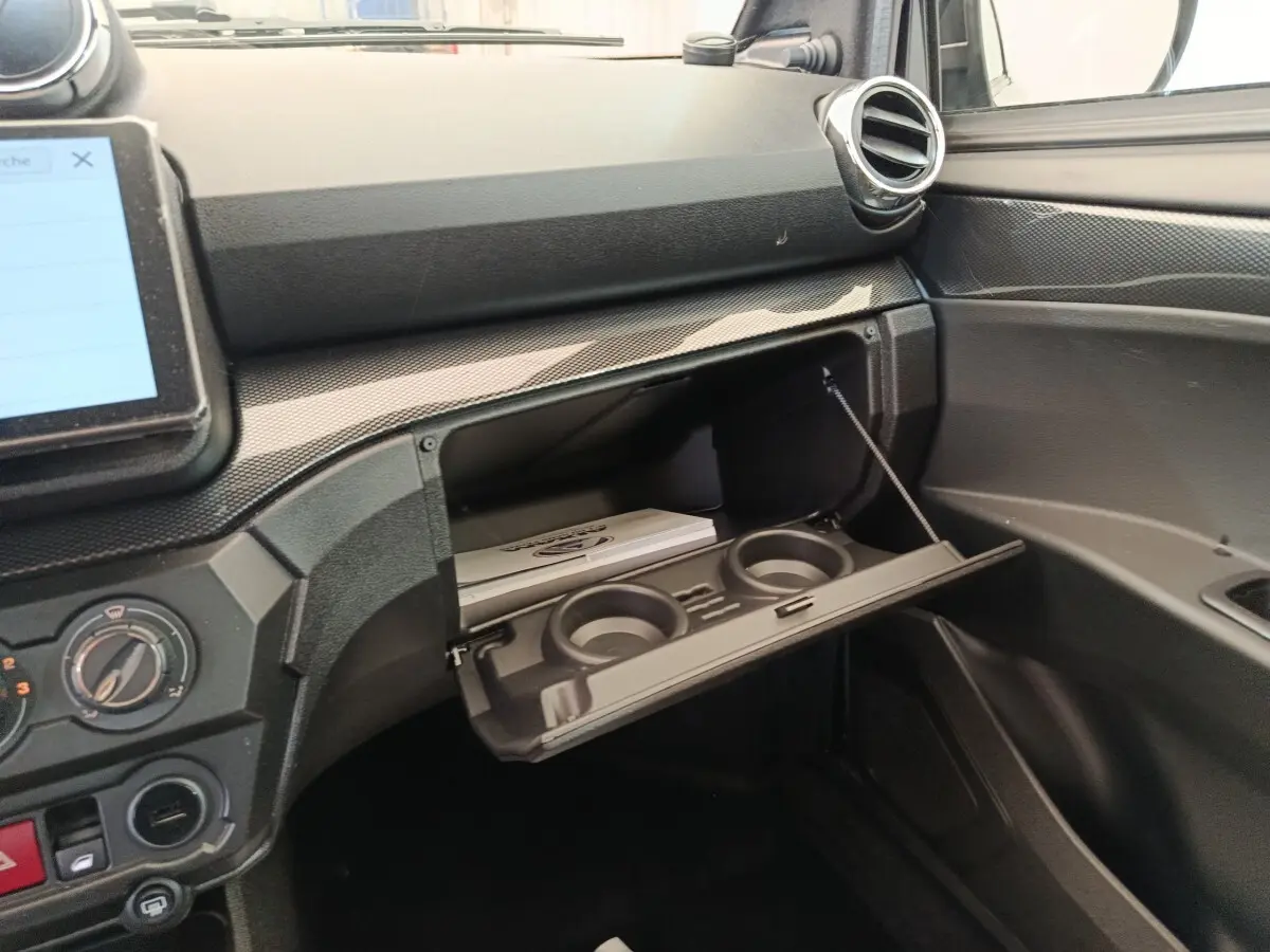 Intérieur de l'AIXAM Ambition 0.5 City Coupe GTI 2026, vue sur la boîte à gants ouverte avec porte-gobelets intégrés.