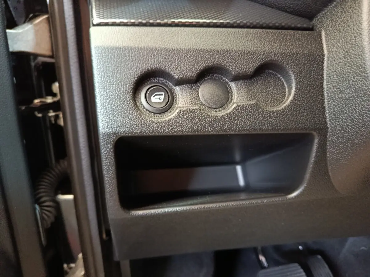 Détail intérieur montrant le bouton d'ouverture du coffre sur le tableau de bord noir côté conducteur de l'AIXAM Ambition 2026.