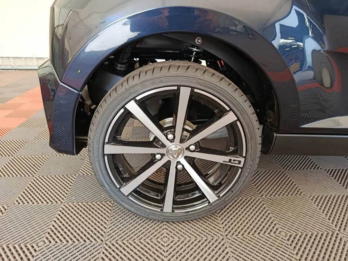 Gros plan sur la roue arrière droite noire d'une Aixam Ambition 0.5 City Coupe GTI avec jante GT en aluminium.