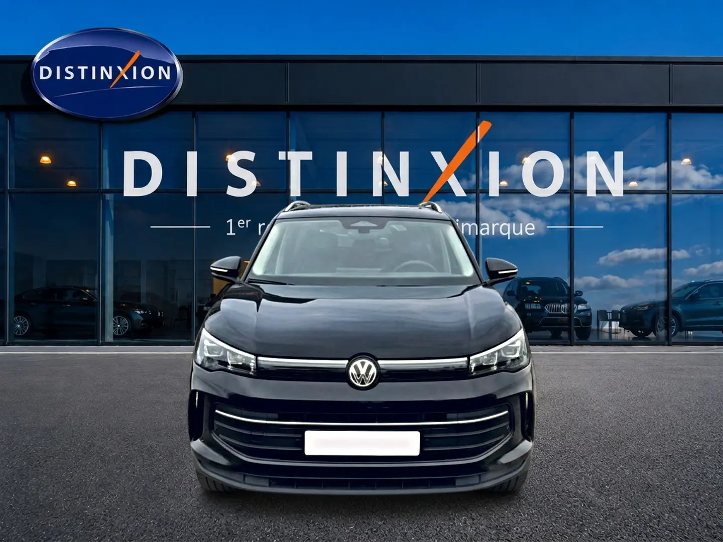 Vue frontale d'un Volkswagen Tiguan noir 2025 avec calandre large et logo VW centré devant un showroom Distinxion.