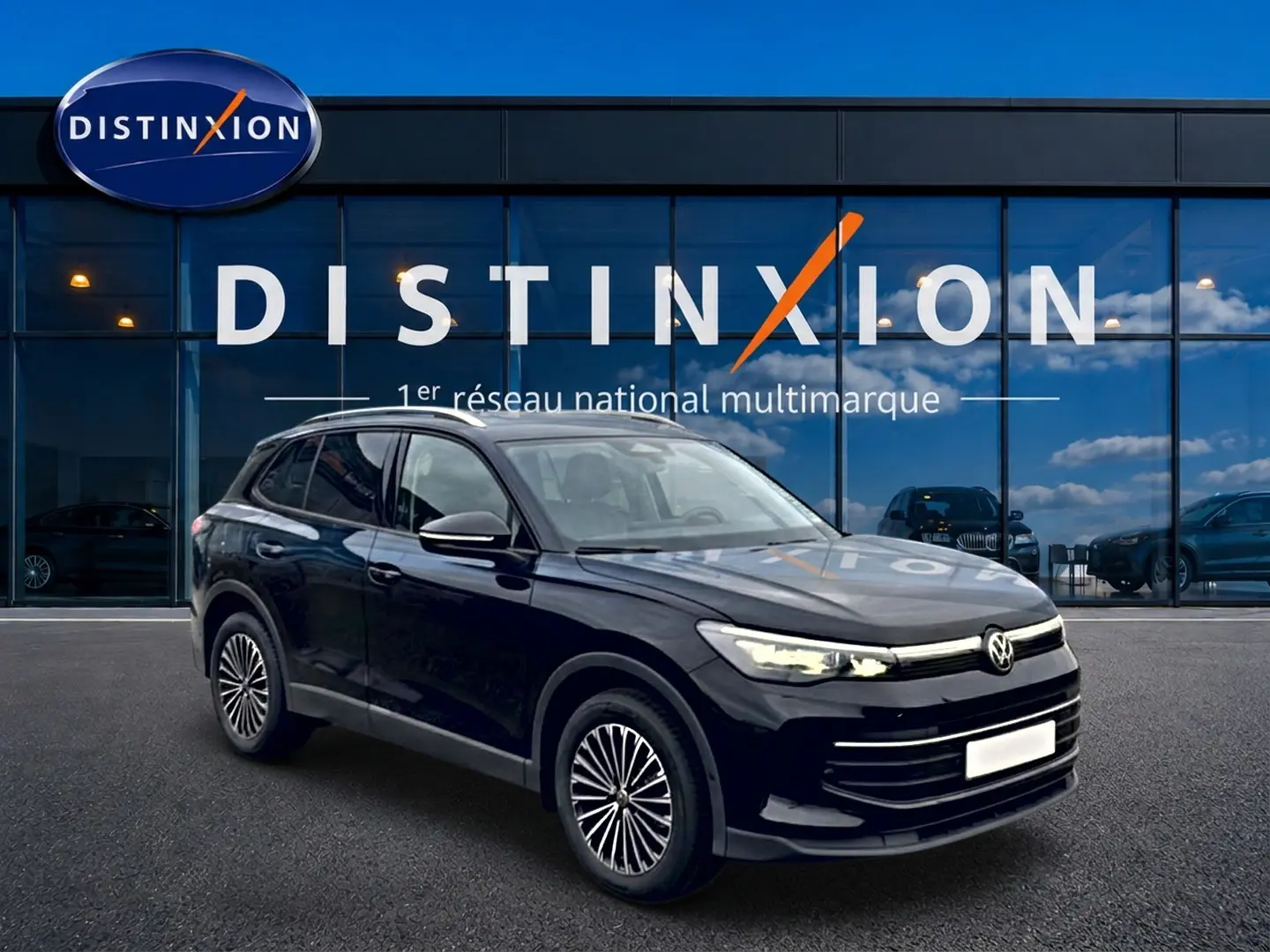 Volkswagen Tiguan 2025 noir en 3/4 avant droit, avec jantes spécifiques et phares LED allumés devant un showroom Distinxion.