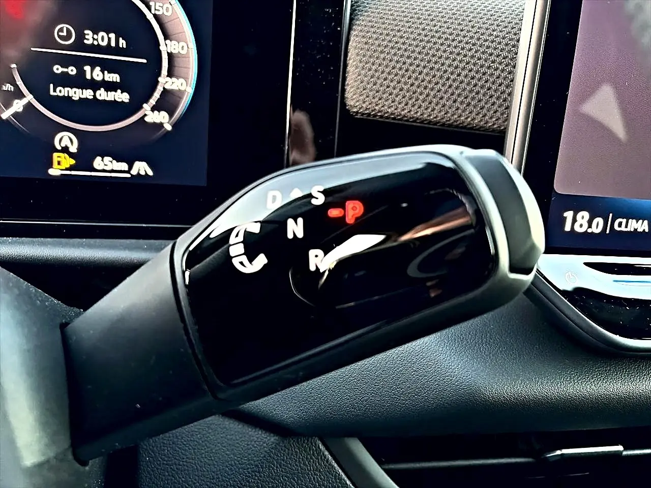 Gros plan sur le levier de vitesses automatique noir brillant du Volkswagen T-Roc 1.5 etsi 150 R-Line 2026 avec affichage digital en arrière-plan.