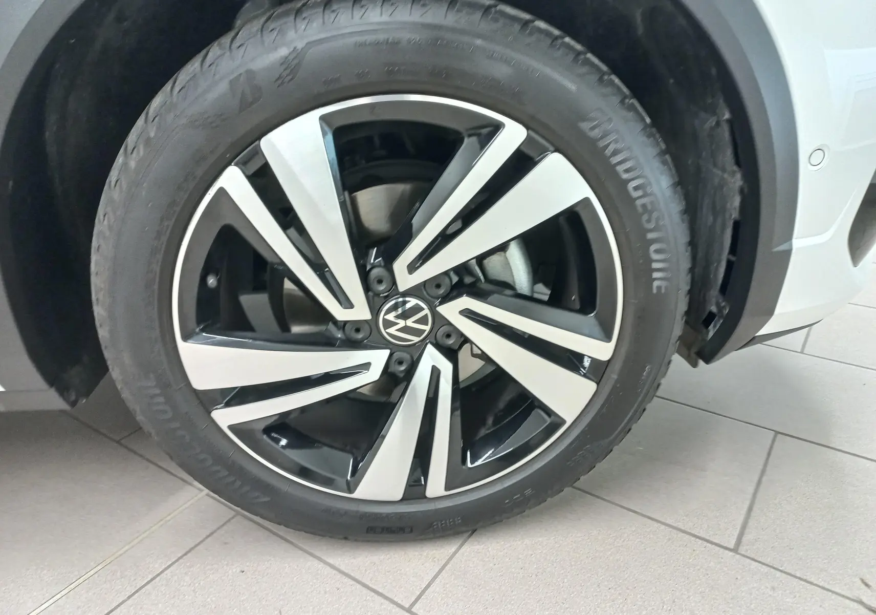 Gros plan sur la roue avant droite du Volkswagen T-Roc blanc pur, jante alliage noir et argentée au design moderne.