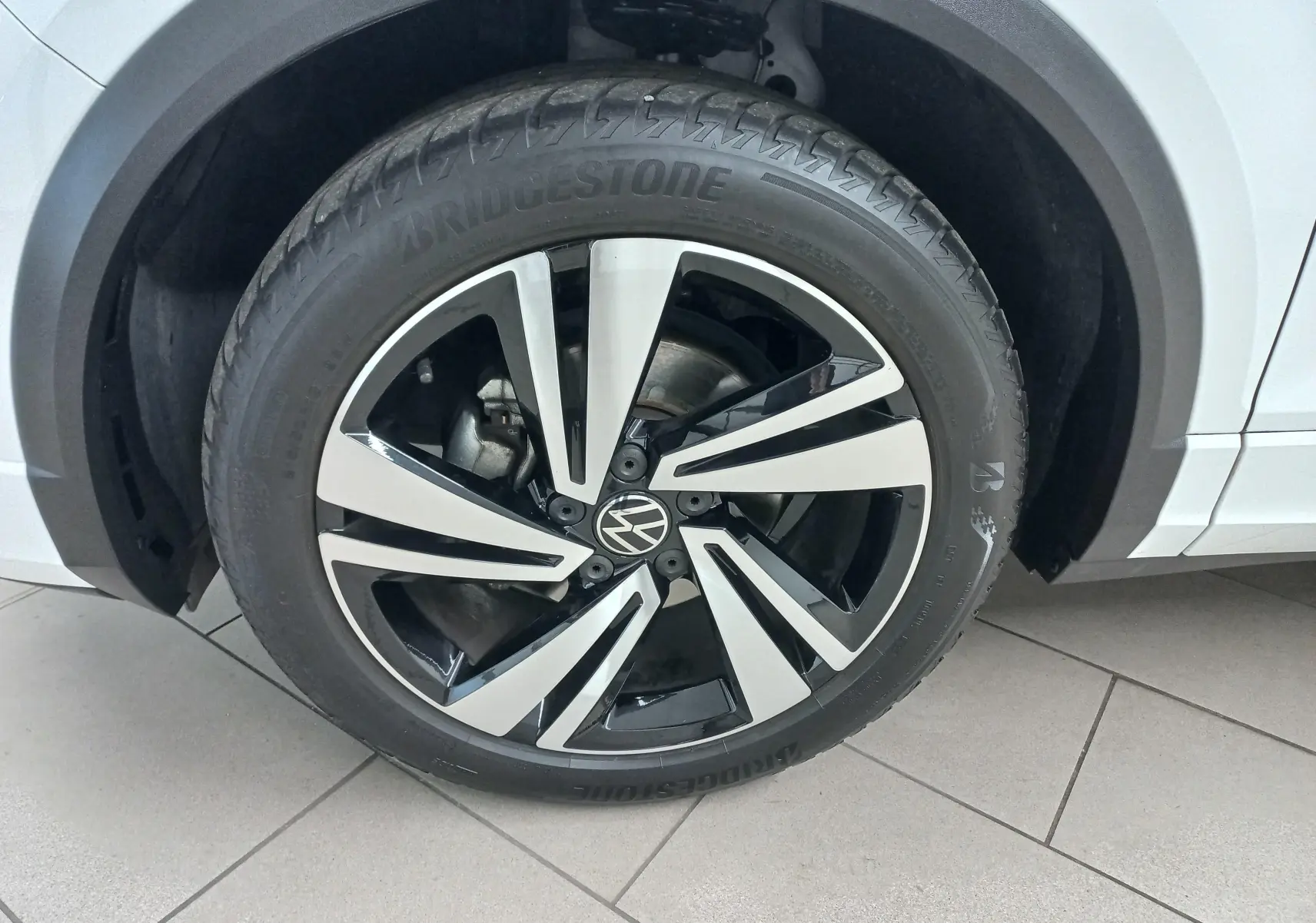 Gros plan sur la roue avant droite du Volkswagen T-Roc blanc pur 2025 avec jante alliage bicolore et pneu Bridgestone.