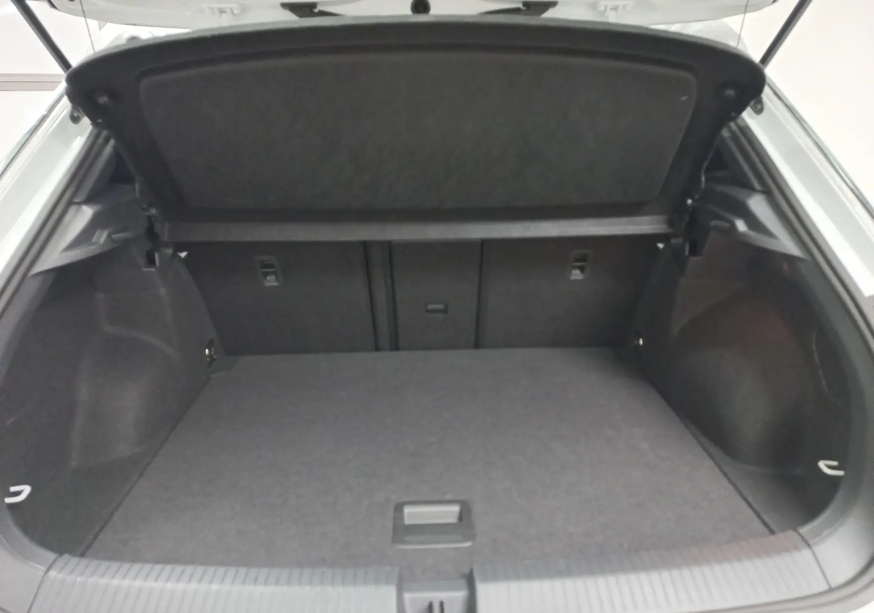 Coffre ouvert du Volkswagen T-Roc blanc pur, vue arrière montrant l’espace de chargement vide et la tablette de séparation.