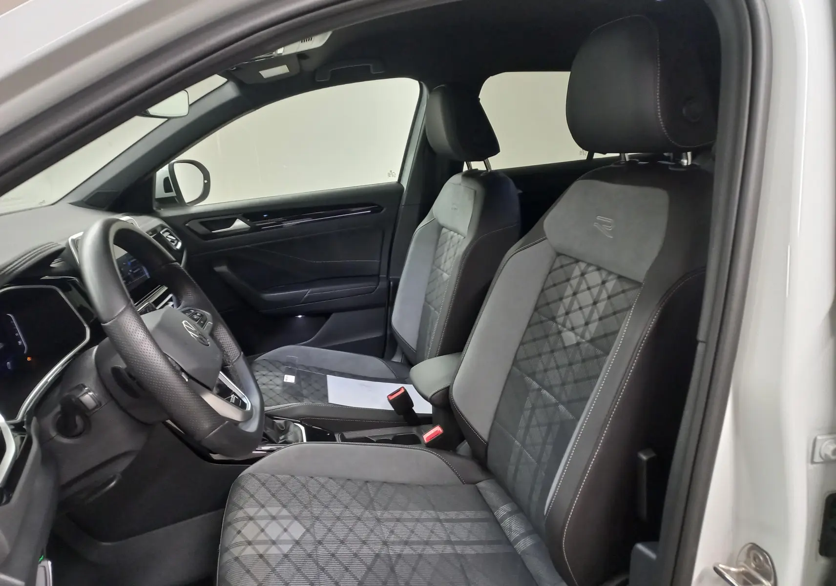Vue intérieure côté conducteur du Volkswagen T-Roc blanc pur 2025, sièges R-Line en tissu et alcantara avec surpiqûres.