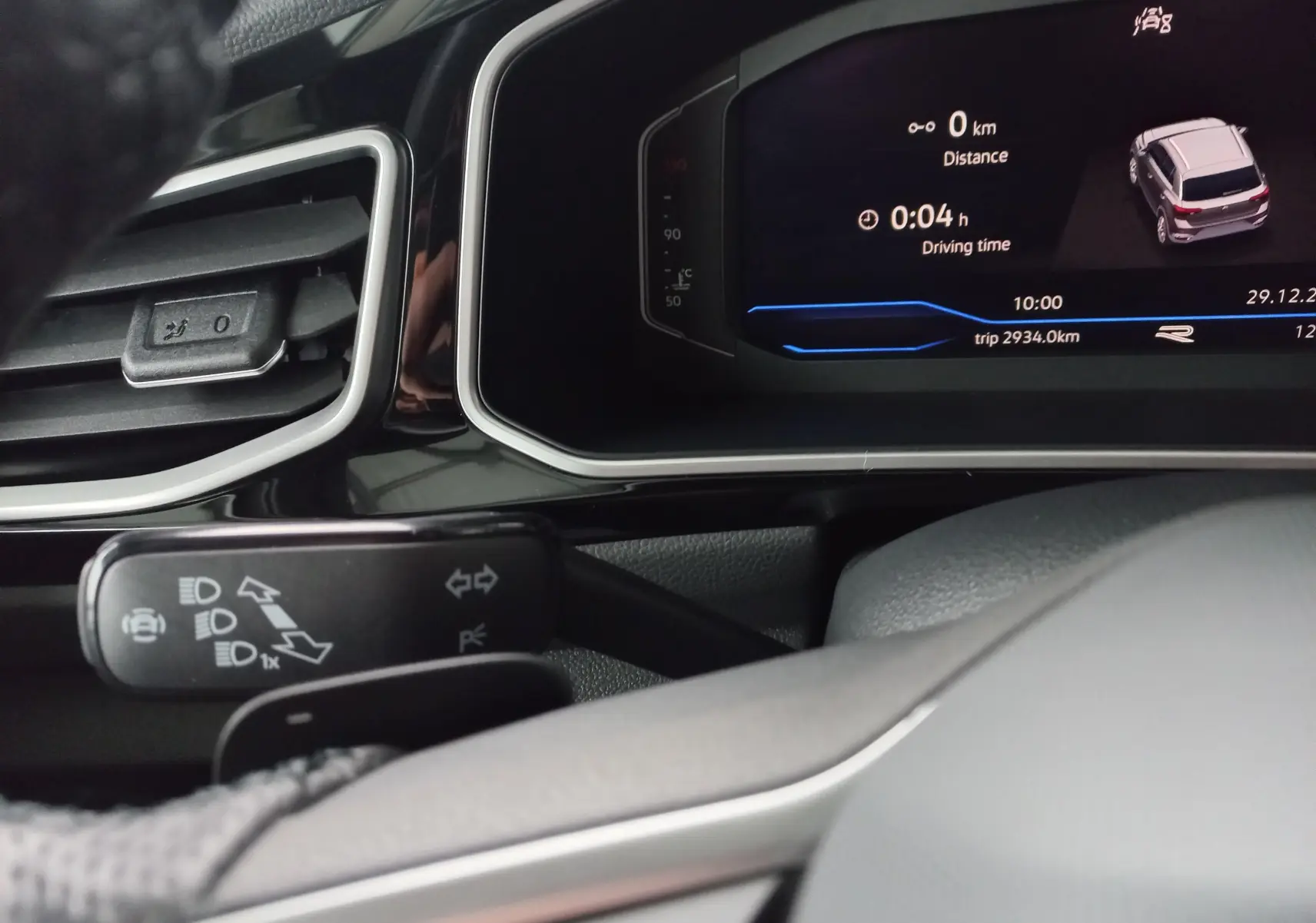 Vue rapprochée du tableau de bord numérique du Volkswagen T-Roc blanc, affichant l'ordinateur de bord et les commandes d'éclairage.