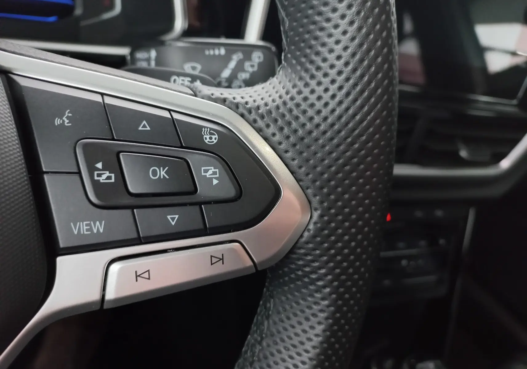 Gros plan sur les commandes gauche du volant en cuir perforé du Volkswagen T-Roc blanc, avec bouton chauffant visible.