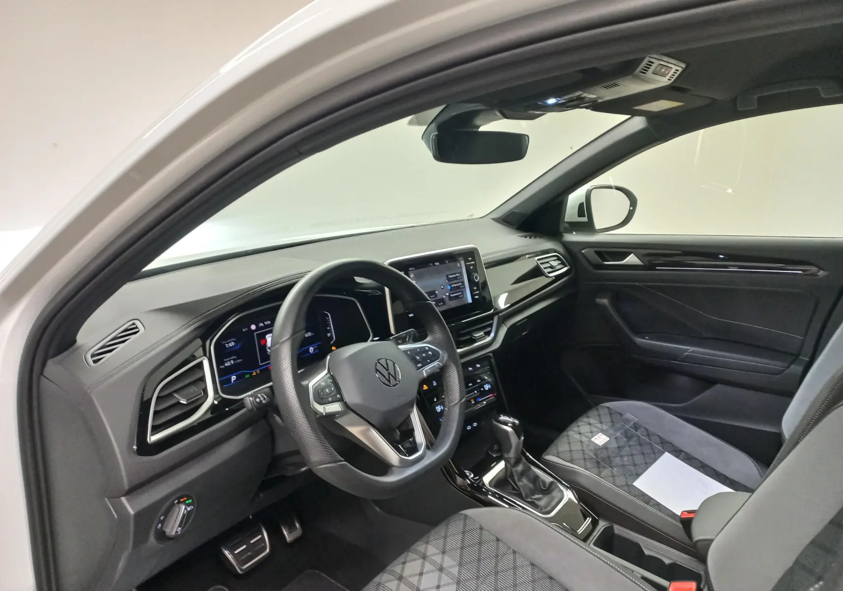 Vue intérieure côté conducteur du Volkswagen T-Roc blanc pur 2025, avec volant chauffant et tableau de bord digital.