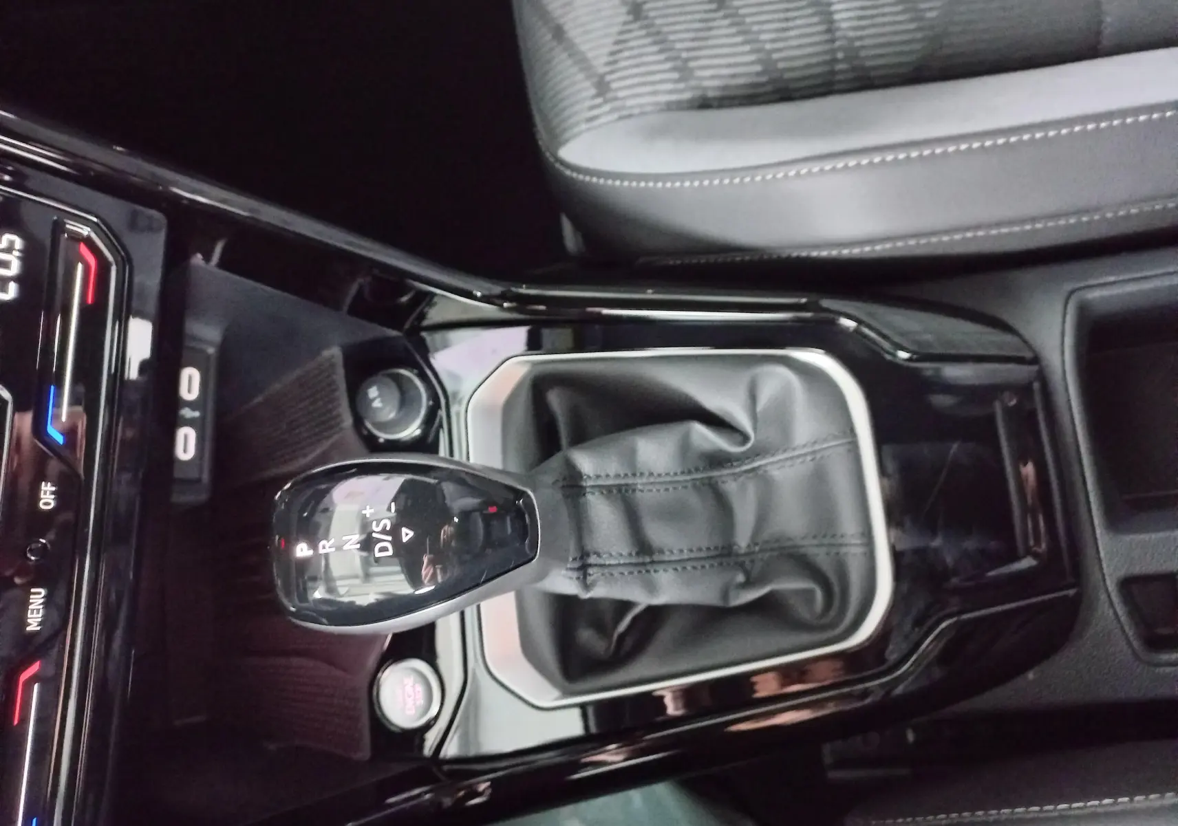 Vue rapprochée de la console centrale du Volkswagen T-Roc blanc, mettant en valeur le levier de vitesse automatique et le siège tissu gris.