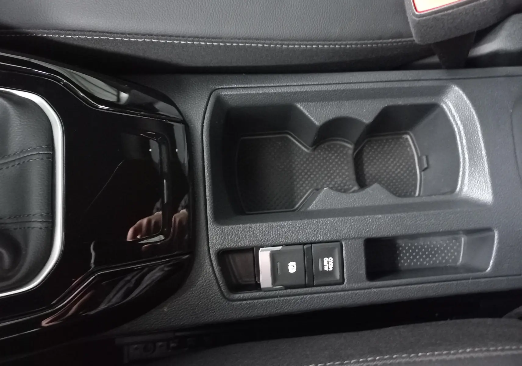 Vue rapprochée de la console centrale noire du Volkswagen T-Roc 1.5 TSI R-Line avec porte-gobelets et frein à main électronique.