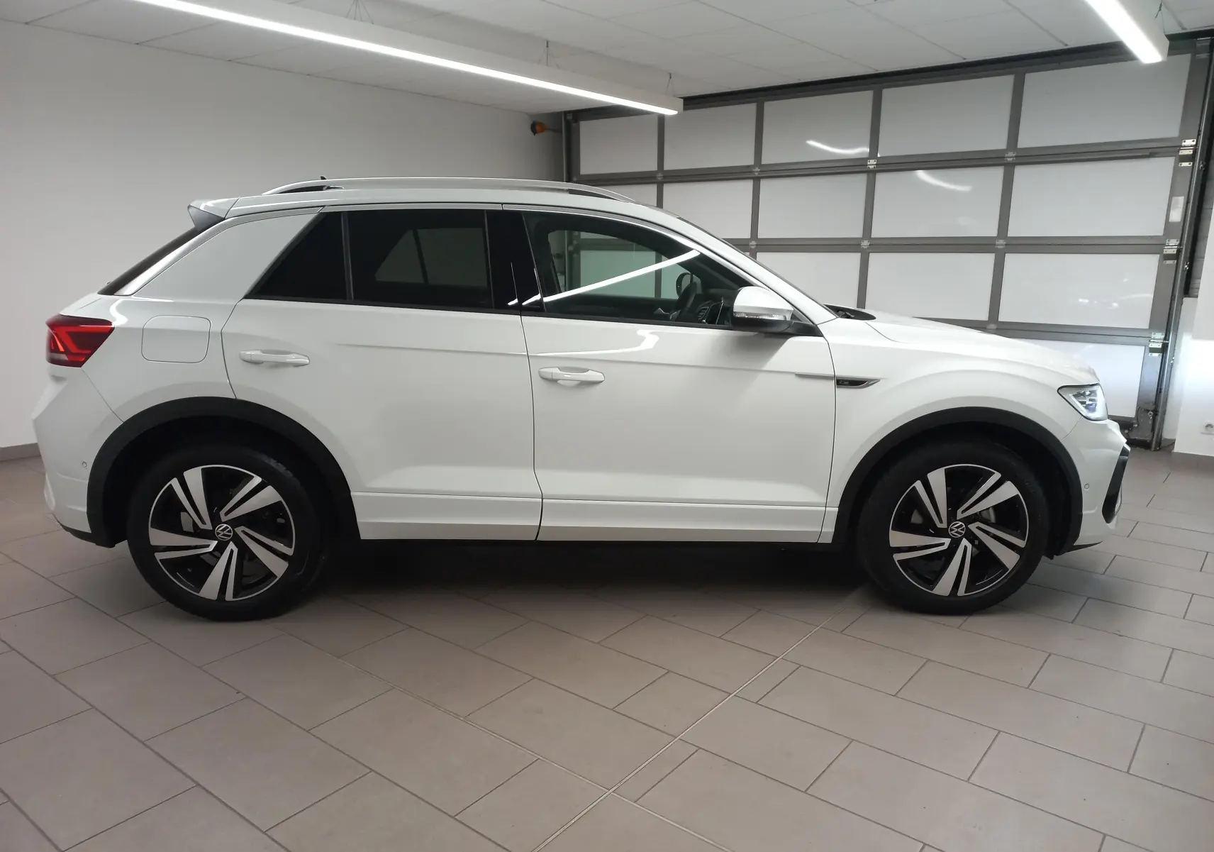 Volkswagen T-Roc blanc pur vu de profil côté gauche dans un garage, avec jantes noires et détails R-Line.