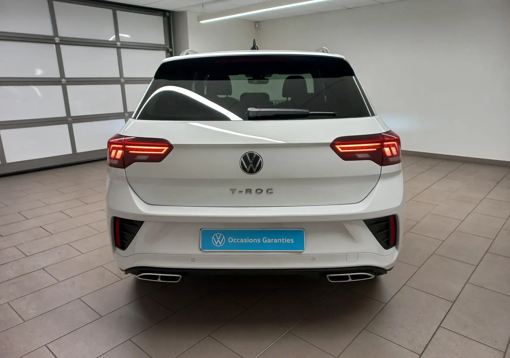 Vue arrière d'un Volkswagen T-Roc blanc pur 2025 avec feux LED allumés et double sortie d'échappement chromée.