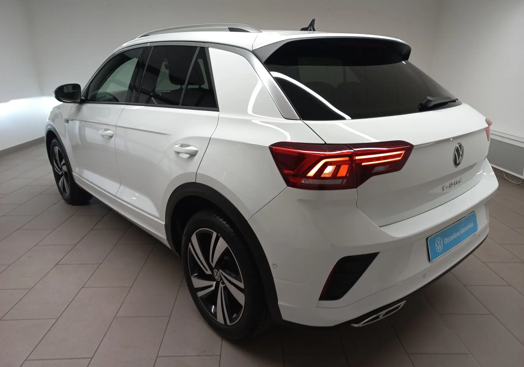 Volkswagen T-Roc blanc pur en vue 3/4 arrière droit, feux LED allumés et jantes alliage distinctives.