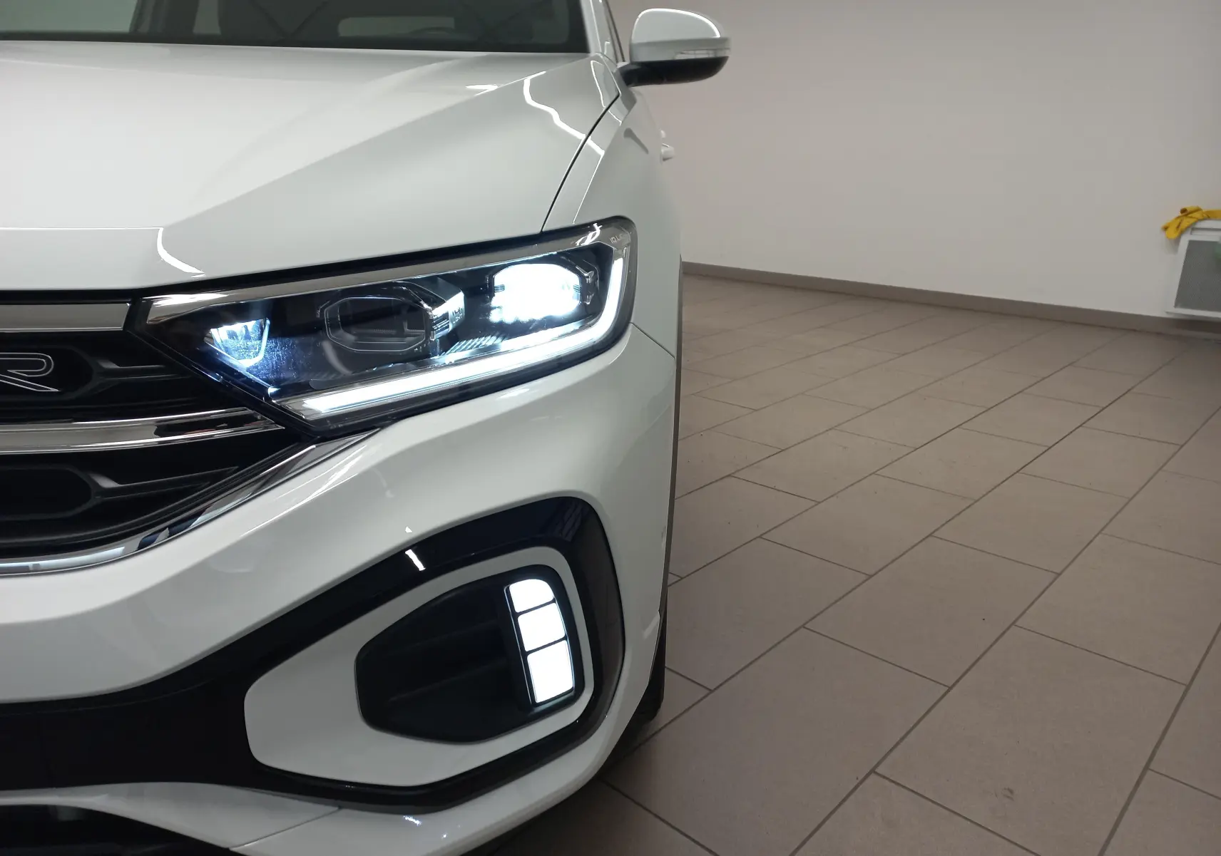 Gros plan sur l'avant droit du Volkswagen T-Roc blanc pur 2025 avec phares et feux LED allumés.