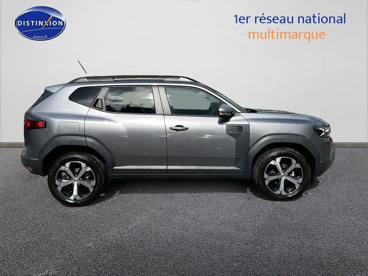 Profil droit du Dacia Duster 2025 gris schiste avec jantes alu et barres de toit visibles sur fond neutre.