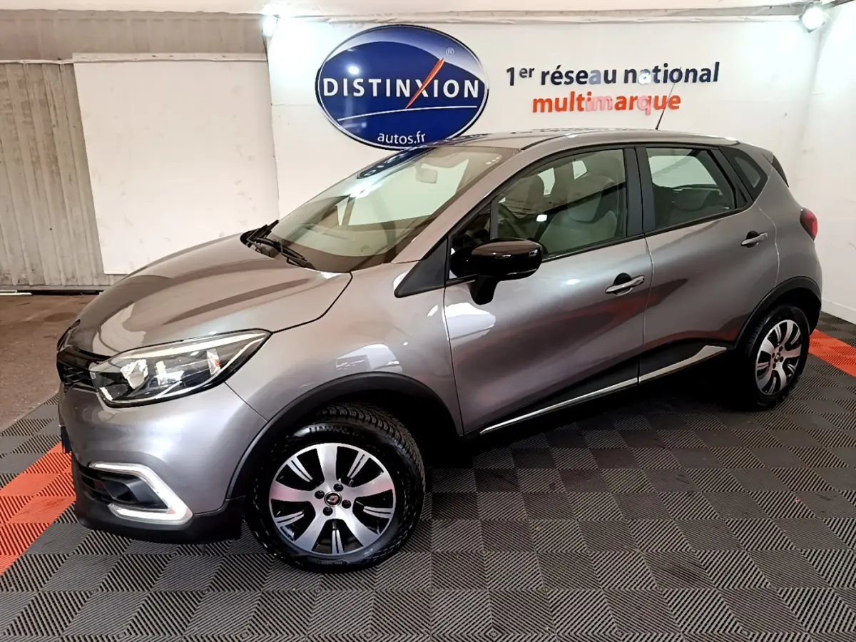 Renault Captur Business gris foncé vu en 3/4 avant droit dans un showroom avec logo Distinxion en arrière-plan.