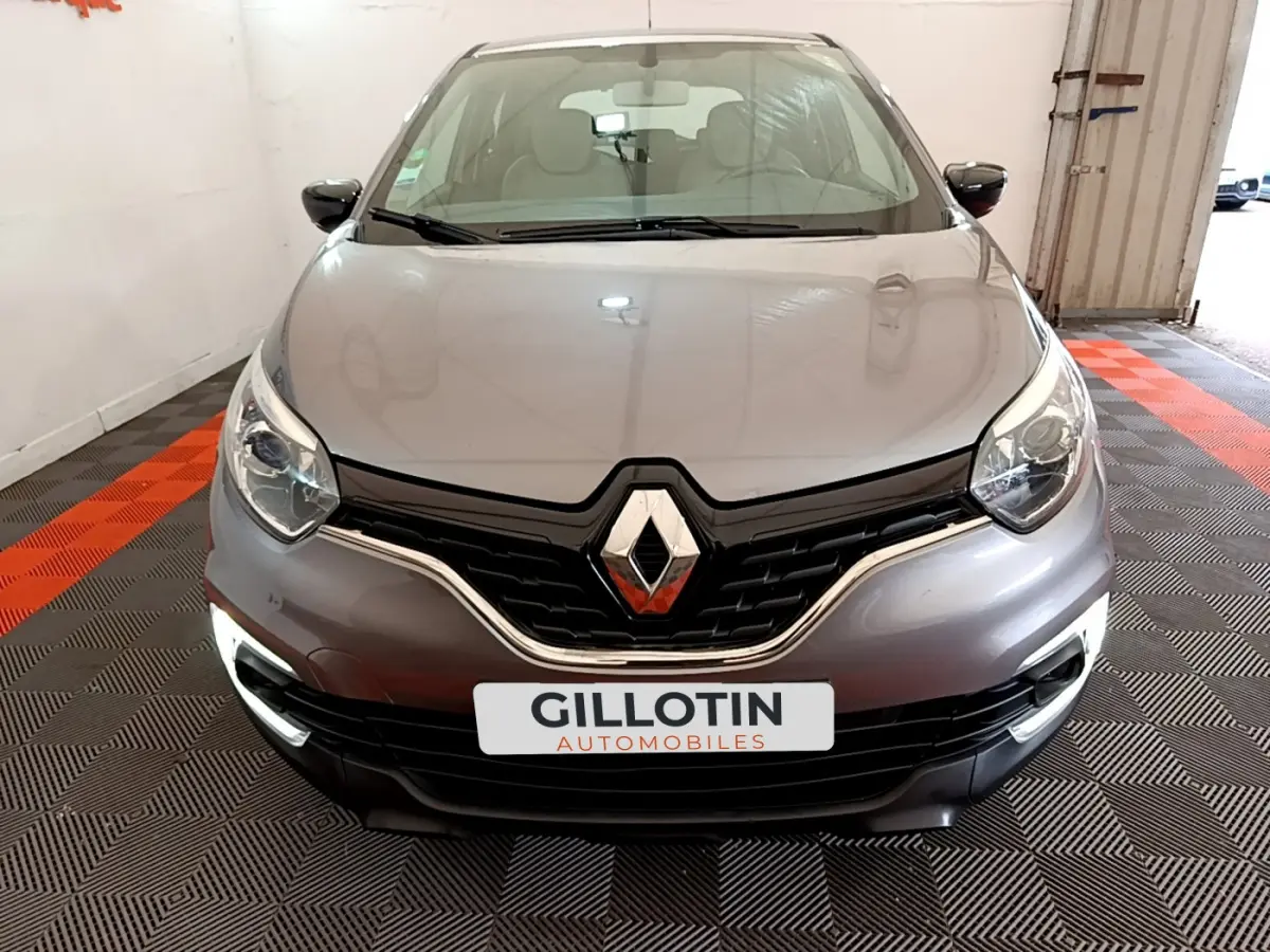 Vue avant d'une Renault Captur gris foncé avec phares allumés et calandre noire brillante dans un garage.