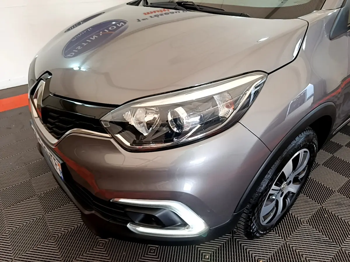 Vue 3/4 avant droit d'un Renault Captur Business gris foncé, mettant en valeur ses phares ellipsoïdaux et sa calandre chromée.