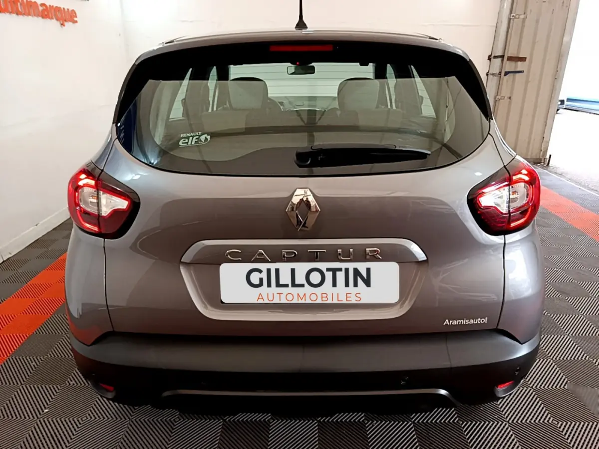 Vue arrière d'un Renault Captur gris foncé 2018 avec feux arrière allumés et logo Renault bien visible.