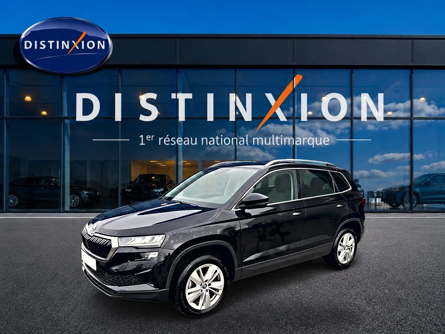 SKODA KAROQ noir 2025 en 3/4 avant droit, avec jantes alu et barres de toit visibles devant un showroom Distinxion.