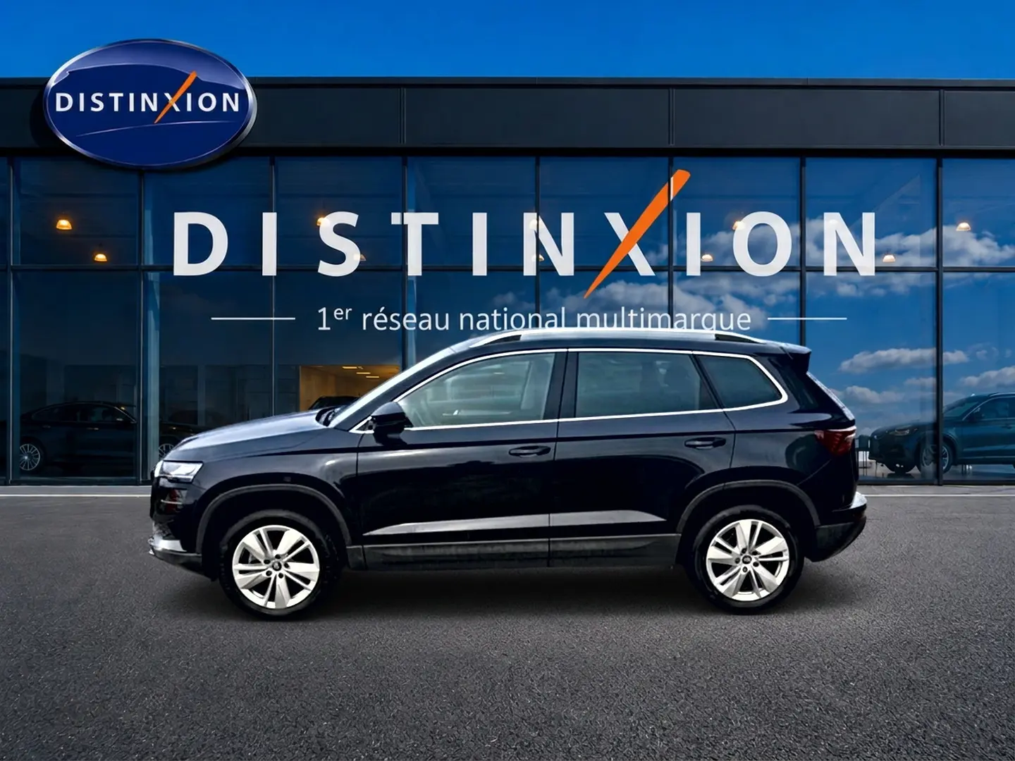 Profil côté gauche d'un Skoda Karoq noir 2025 garé devant une vitrine avec logo Distinxion.