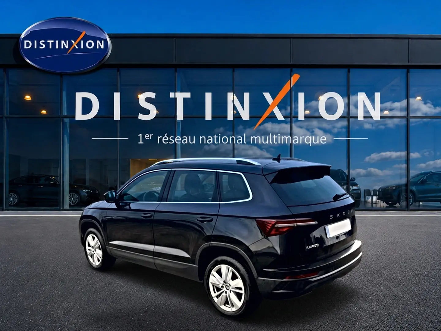 Vue 3/4 arrière droite d'un Skoda Karoq noir 2025 avec jantes alu, barres de toit et becquet arrière visible.