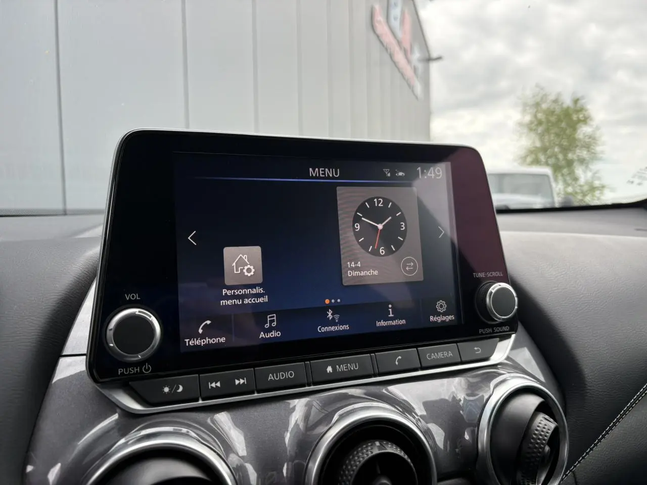 Écran tactile central du Nissan Juke 2024 affichant le menu principal avec commandes audio et caméra, intérieur noir.