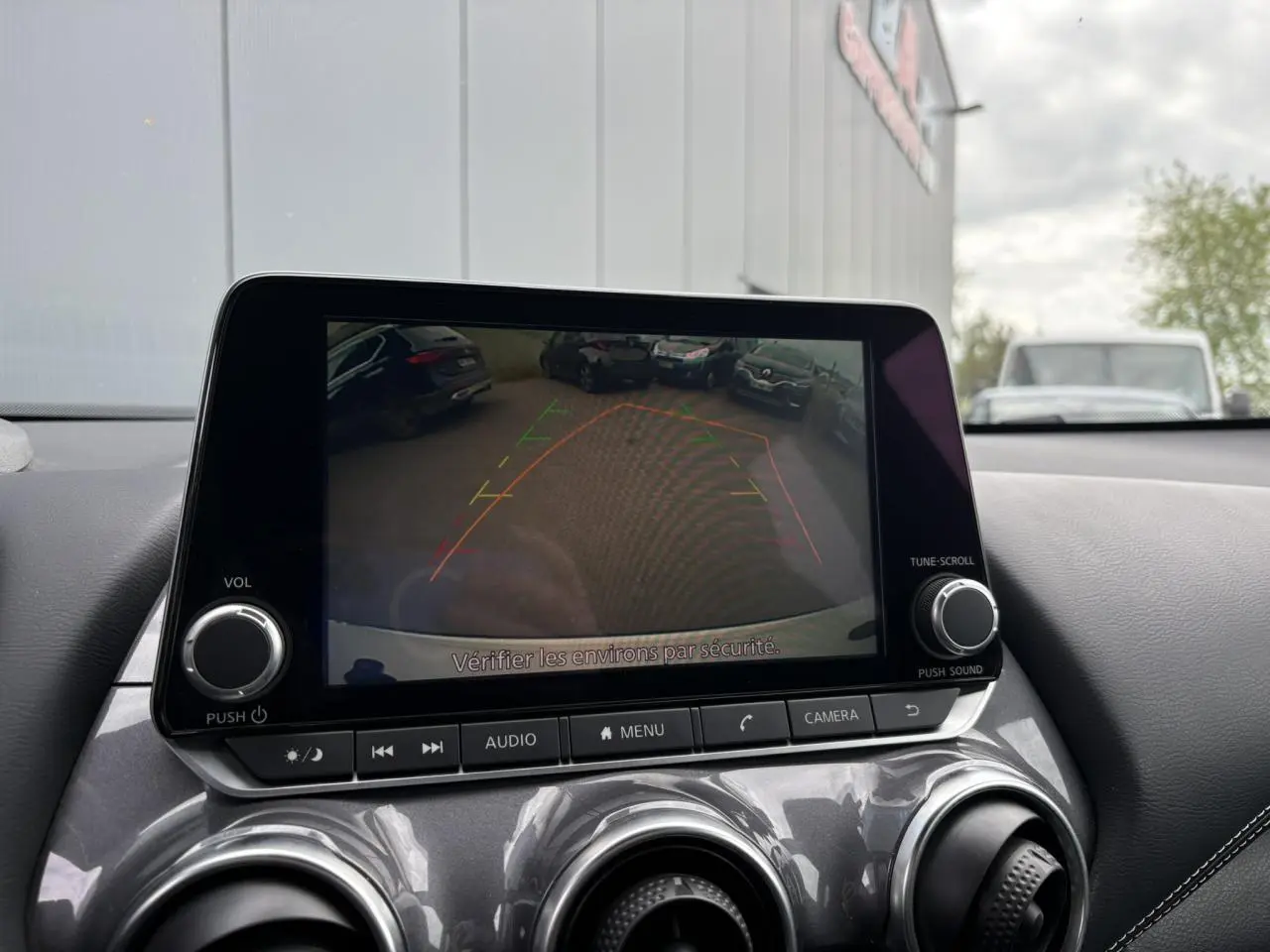 Écran central du Nissan Juke blanc perle 2024 montrant la caméra de recul avec lignes d'aide au stationnement.