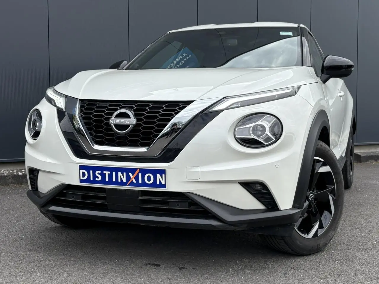 Nissan Juke blanc perle en 3/4 avant droit, avec calandre noire et jantes alliage noires distinctives.