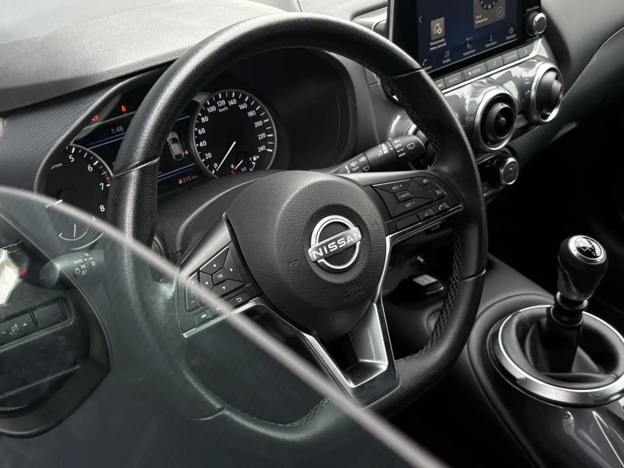 Vue rapprochée de l'intérieur du Nissan Juke blanc perle 2024, volant multifonction et levier de vitesse manuel visibles.