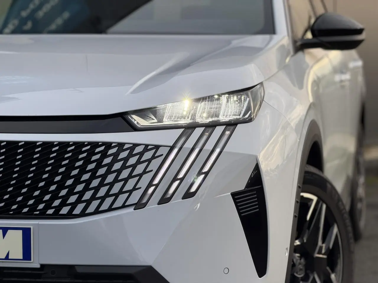 Gros plan sur l'avant droit du Peugeot 3008 blanc Okénite, mettant en valeur les phares LED et la calandre distinctive.