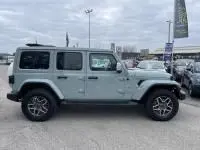 Vue de profil droit d'un Jeep Wrangler Unlimited vert métal 2023 hybride rechargeable sur un parking extérieur.