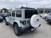Vue 3/4 arrière droite d'une Jeep Wrangler Unlimited 2023 vert métal, hybride rechargeable, avec roue de secours blanche et attelage.