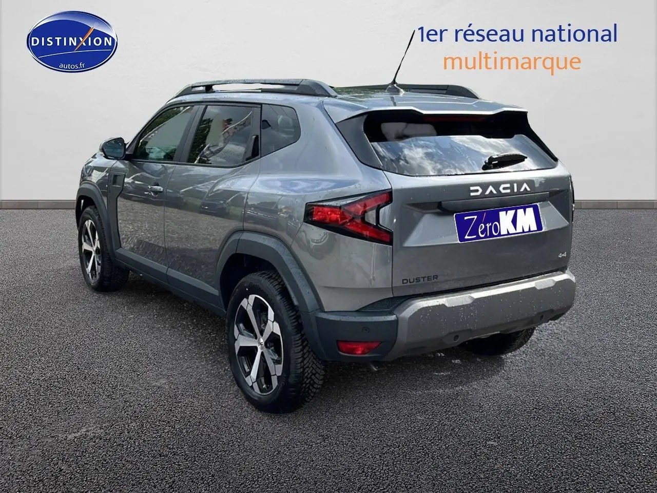 Vue 3/4 arrière droite du Dacia Duster gris schiste avec jantes alu et barres de toit visibles.